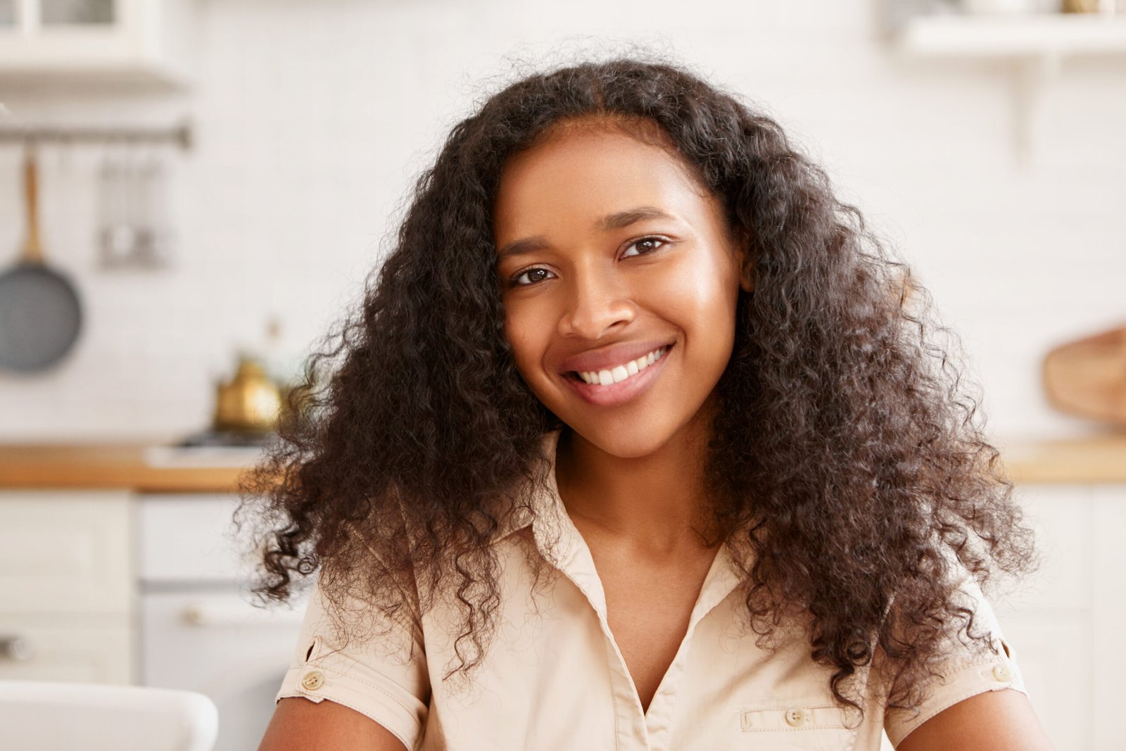 People, beauty, ethnicity, femininity and positive human emotions. Cute beautiful young African female with charming beaming smile, rejoicing at good news, having breakfast in cozy kitchen